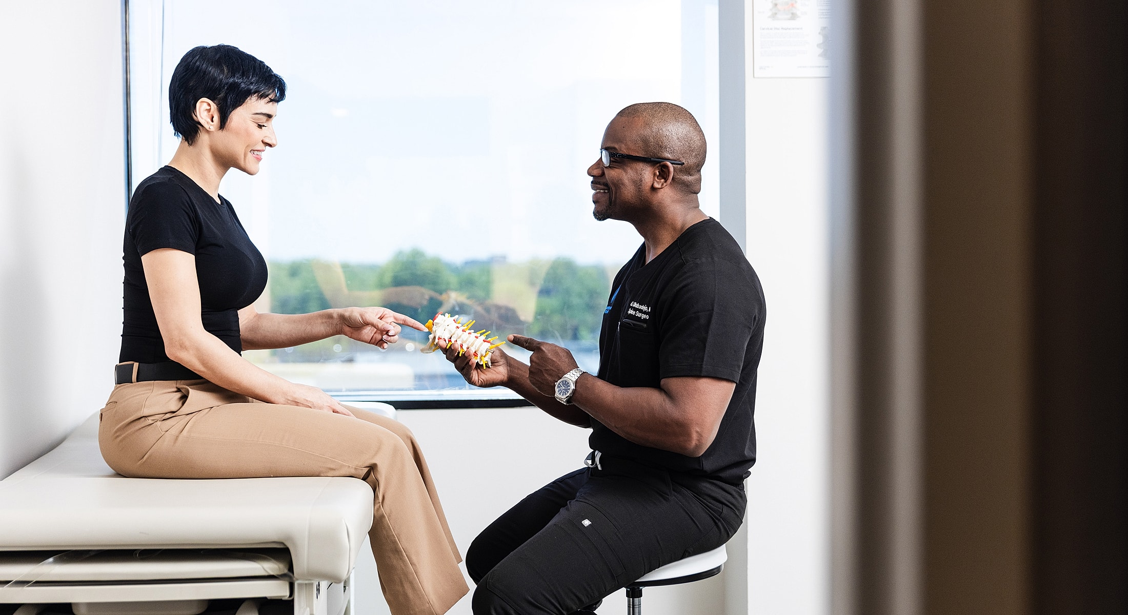 anterior cervical discectomy patient interacting with a spine surgeon, both pointing to a model spine.
