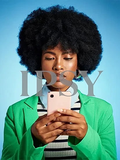 Woman with afro using smartphone in green blazer.