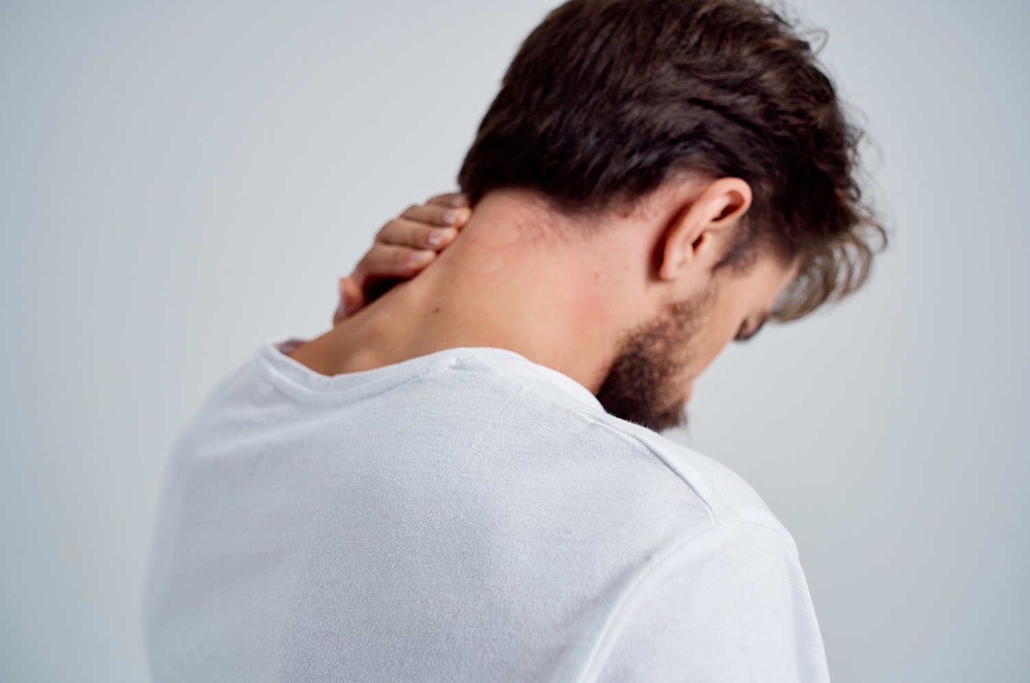 Man rubbing his neck in white shirt.