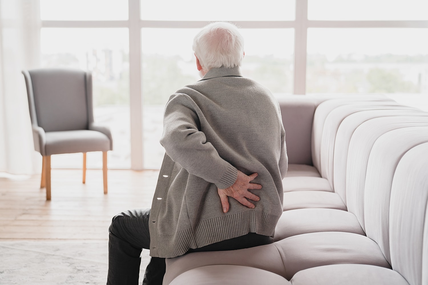 Elderly man experiencing back pain on sofa.