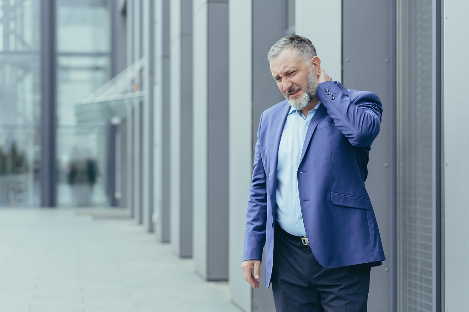 Businessman holding his neck outside a modern building.
