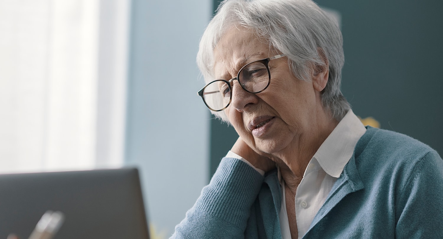 Elderly woman experiencing discomfort while using laptop.