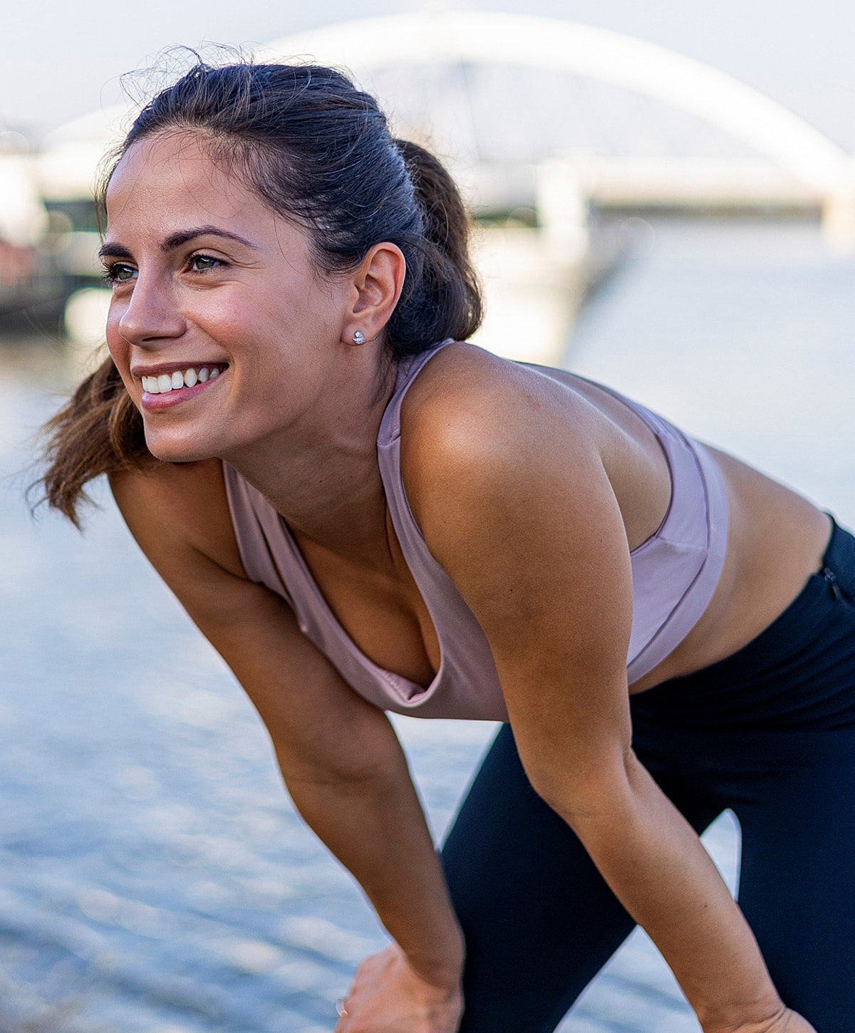 revision spine surgery patient model in a sports bra and yoga leggings exercising by the water, smiling and relaxed.