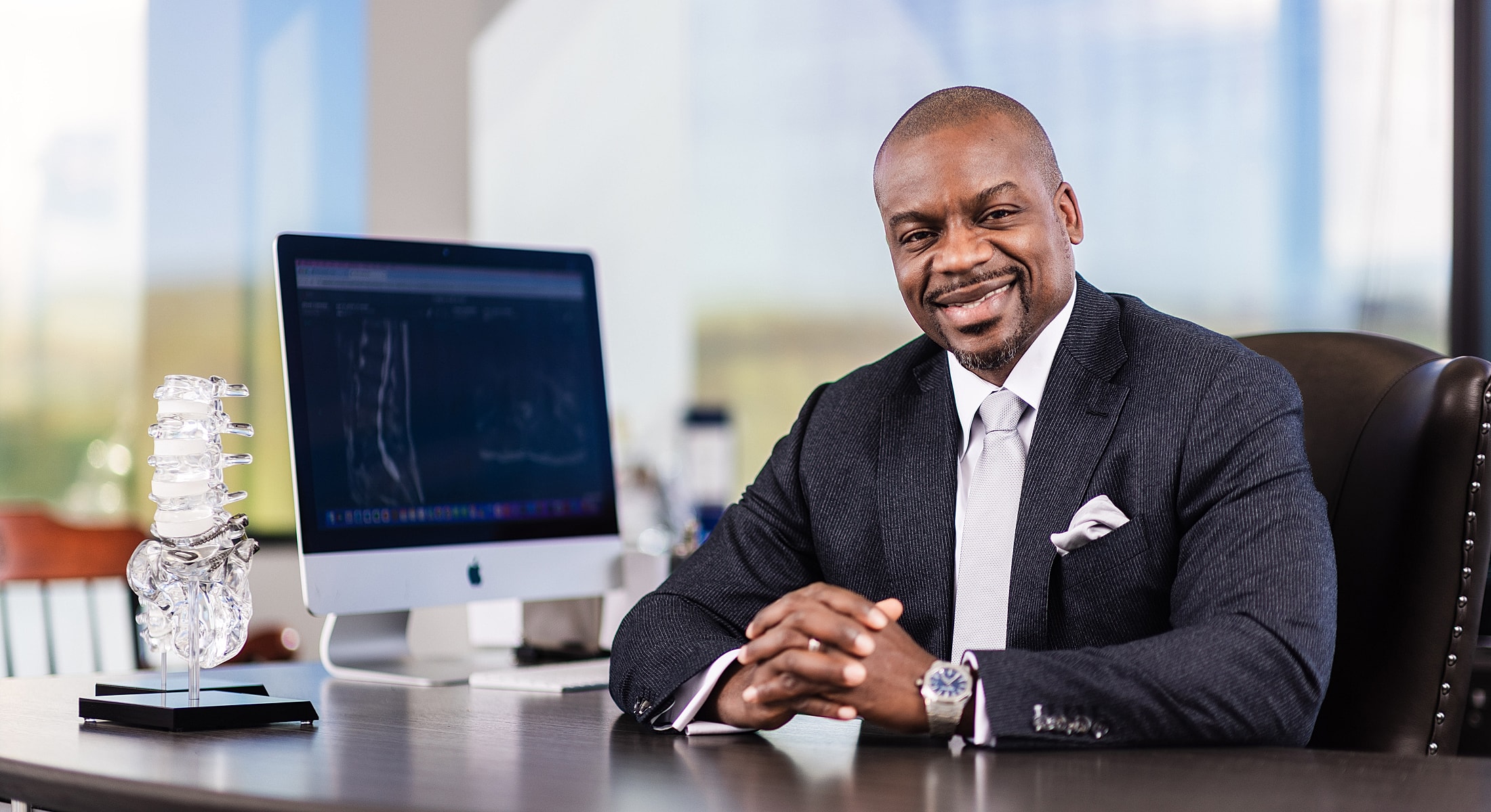 Smiling professional with spinal model and computer.