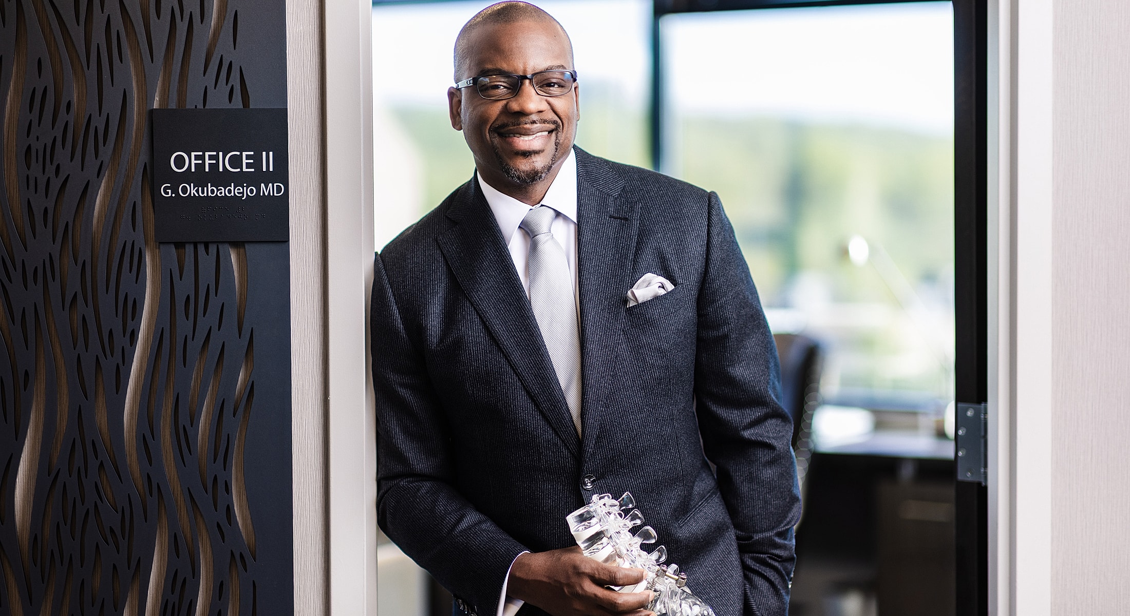 nj & nyc spine surgeon dr. okubadejo standing in office doorway, smiling confidently.