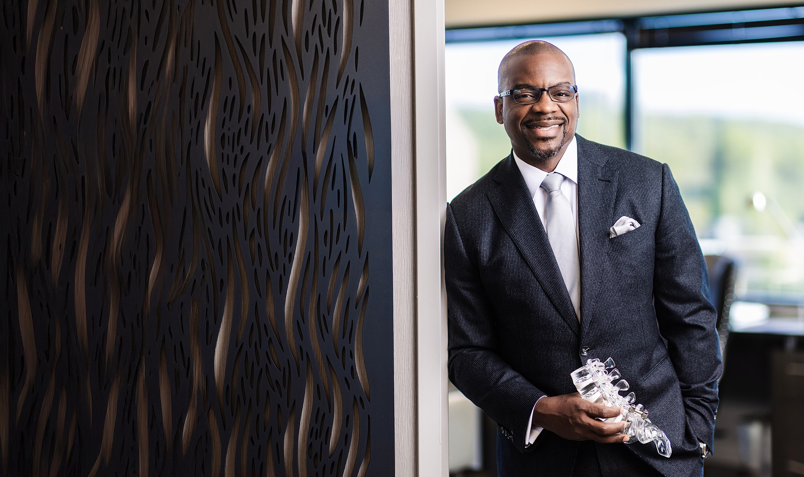 Smiling spine surgeon in a suit holding a glass object.